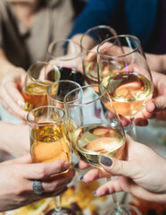 Group of guests celebrate and raise glasses, toasting and cheering with alcohol glasses with wine and champagne in the restaurant on corporate christmas birthday party event or wedding celebration