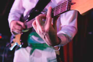 Obraz premium Concert view of an electric guitar player with vocalist and rock band performing in a club, male musician guitarist on stage with audience in a crowded concert hall arena