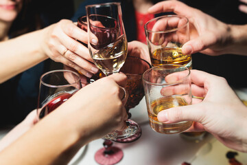Group of guests celebrate and raise glasses, toasting and cheering with alcohol glasses with wine and champagne in the restaurant on corporate christmas birthday party event or wedding celebration - obrazy, fototapety, plakaty