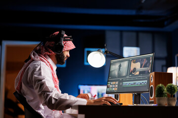 Arab guy director sat at table, attentively working on film post-production. Muslim video editor in...