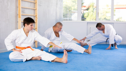 Group of men of different ages in a white kimono doing muscle stretching before karate or judo...