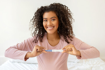 Happy beautiful black woman holding positive pregnancy test