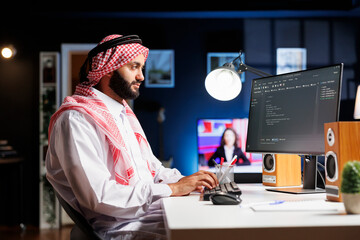 Side-view of Muslim developer writing code on desktop pc, parsing algorithm in a software agency....