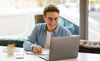 Smiling millennial european guy in glasses, typing on laptop, work, study or online communication