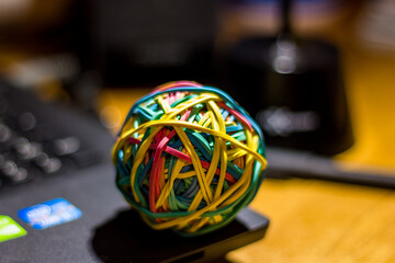 A ball made of multi-colored rubber bands lies on a laptop