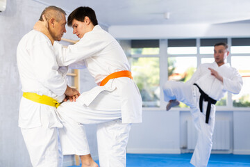 Elderly man and young guy sparring during karate classes in the gym under the guidance of a coach