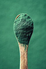 Green spirulina algae powder on a wooden spoon, vertical shot