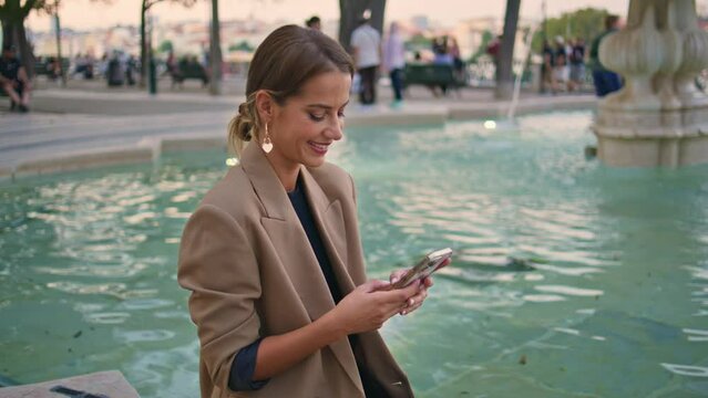 Stylish businesswoman texting mobile phone at evening water fountain zoom on.