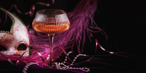 Masquerade ball holiday background. Glass of rose champagne, Venetian carnival mask and feathers on dark burgundy velour background