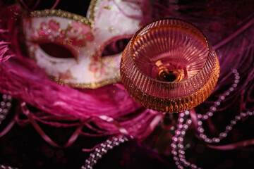 Masquerade ball holiday background. Glass of rose champagne, Venetian carnival mask and feathers on dark burgundy velour background