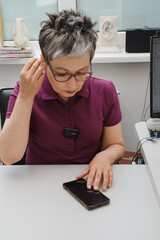 Woman adjusting hearing aid through smartphone. Hearing loss treatment and small device for...