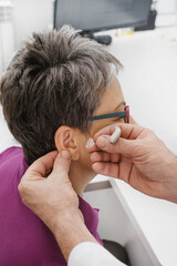 Otolaryngologist puting Modern miniature hearing aids for mid aged woman at modern medical center....