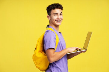 Portrait of handsome smiling teenage boy wearing stylish casual clothes with backpack holding laptop
