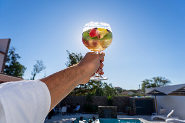 glass elevation towards the sun with white sangria with fruit in the shape of tchin...