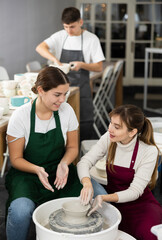 Two young women create clay product on potter's wheel in workshop