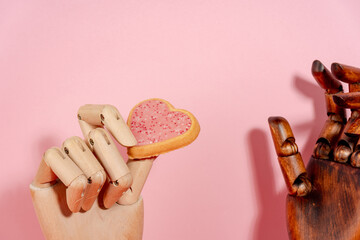  Closeup view wooden mannequin hand giving heart shaped cookie st valentine concept on pink...