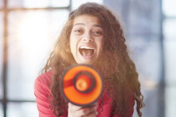 Beautiful girl shouting into a megaphone in a modern office