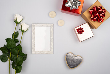 romantic gray background with empty frame in the center with two white roses with candles with gift box and silver plush heart
