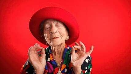 Funny crazy senior elderly woman saying OM, 80s, meditating doing yoga exercise isolated on red background. Concept of youthful old female. - obrazy, fototapety, plakaty