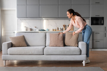 Woman arranging pillows on sofa in a clean living room