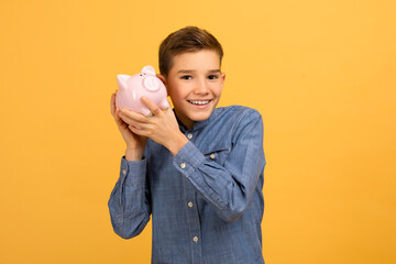 Happy teen boy holding pink piggy bank in hands
