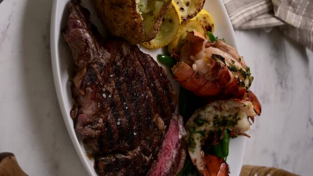 vertical video, surf and turf, ribeye steak and lobster tail on white marble background