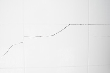 A white tiled wall with water droplets in the bathroom. Broken, cracked tiles. destroyed wall as a...