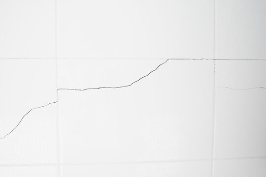 A white tiled wall with water droplets in the bathroom. Broken, cracked tiles. destroyed wall as a result of the earthquake.