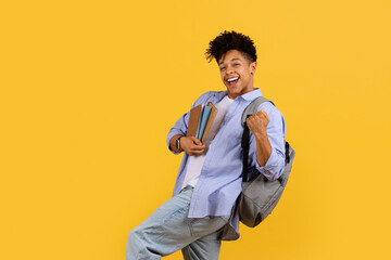 Energetic student with books jumping in excitement on yellow