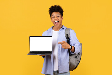 Ecstatic male student pointing at laptop screen on yellow, mockup