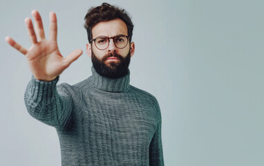 A handsome man with a beard, wearing a sweater and glasses, shows his palm with a serious and negative expression on his face.