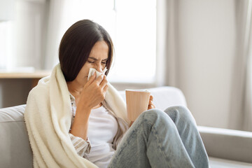 Young woman feeling sick at home, blowing her nose with tissue