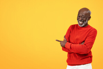 Cheerful senior Black man with a white beard pointing to the side, wearing a bright red sweater