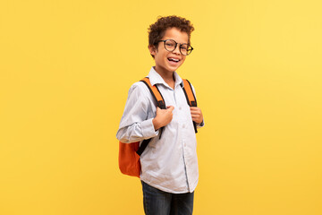 Happy black schoolboy with backpack smiling on yellow backdrop