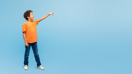Excited boy pointing in the air at free space on blue backdrop