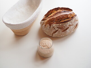Homemade sourdough bread and its fresh leaven and banneton on a white table
