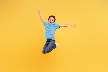 Ecstatic black boy jumping with joy on yellow background