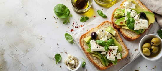 Open sandwich made of slices of sourdough bread with avocado feta cheese kalamata olives olive oil and oregano on a wooden white table close up Vegetarian food. with copy space image