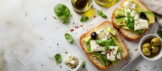 Zelfklevend Fotobehang Open sandwich made of slices of sourdough bread with avocado feta cheese kalamata olives olive oil and oregano on a wooden white table close up Vegetarian food. with copy space image © vxnaghiyev