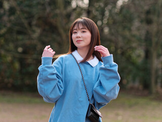Naklejka premium Beautiful young Chinese woman posing in sunny summer forest, wearing blue loose oversized top and miniskirt with small shoulder bag. Emotions, people, beauty, youth and lifestyle portrait.