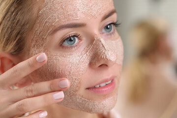 Woman applying face mask on blurred background, closeup. Spa treatments