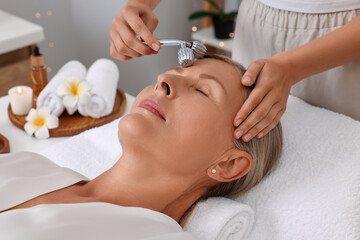 Obraz na płótnie Canvas Woman receiving facial massage with metal roller in beauty salon, closeup