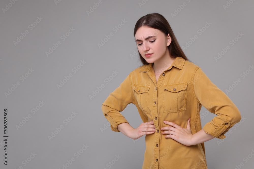 Wall mural Young woman suffering from stomach pain on grey background. Space for text