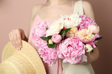 Woman with bouquet of beautiful peonies in bag and hat on beige background, closeup