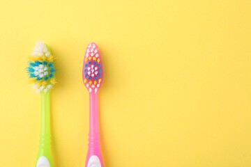 Colorful plastic toothbrushes on yellow background, flat lay. Space for text