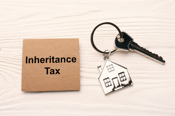 Inheritance Tax. Card and key with metallic key chain in shape of house on white wooden table, flat...