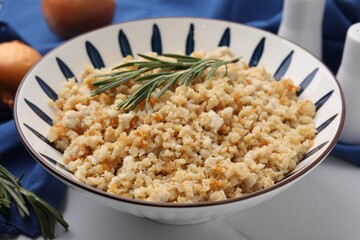 Fried ground meat in bowl and rosemary on white tiled table, closeup