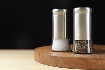 Salt and pepper shakers on wooden table against black background, space for text