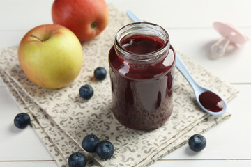 Tasty baby food in jar, blueberries and apples on white table