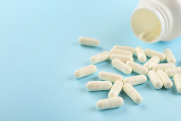 Bottle and vitamin capsules on light blue background, closeup. Space for text